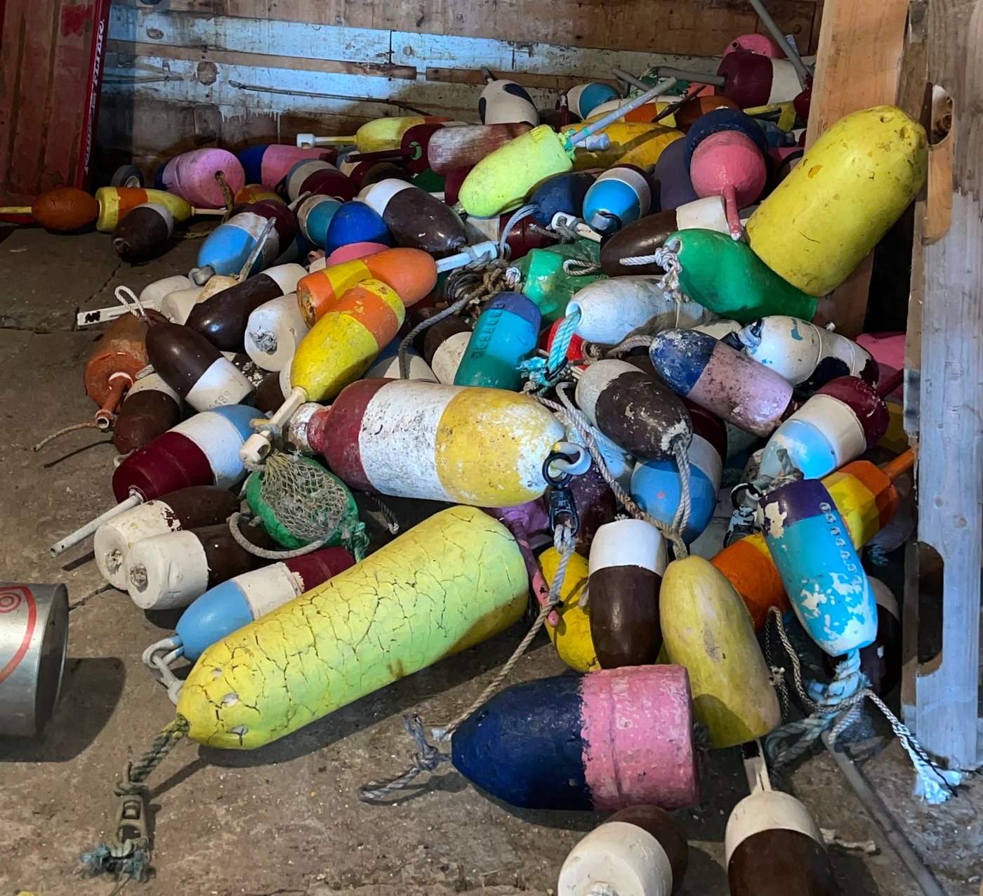 A pile of painted wooden lobster buoys in a Maine shed, each in a different color combination.